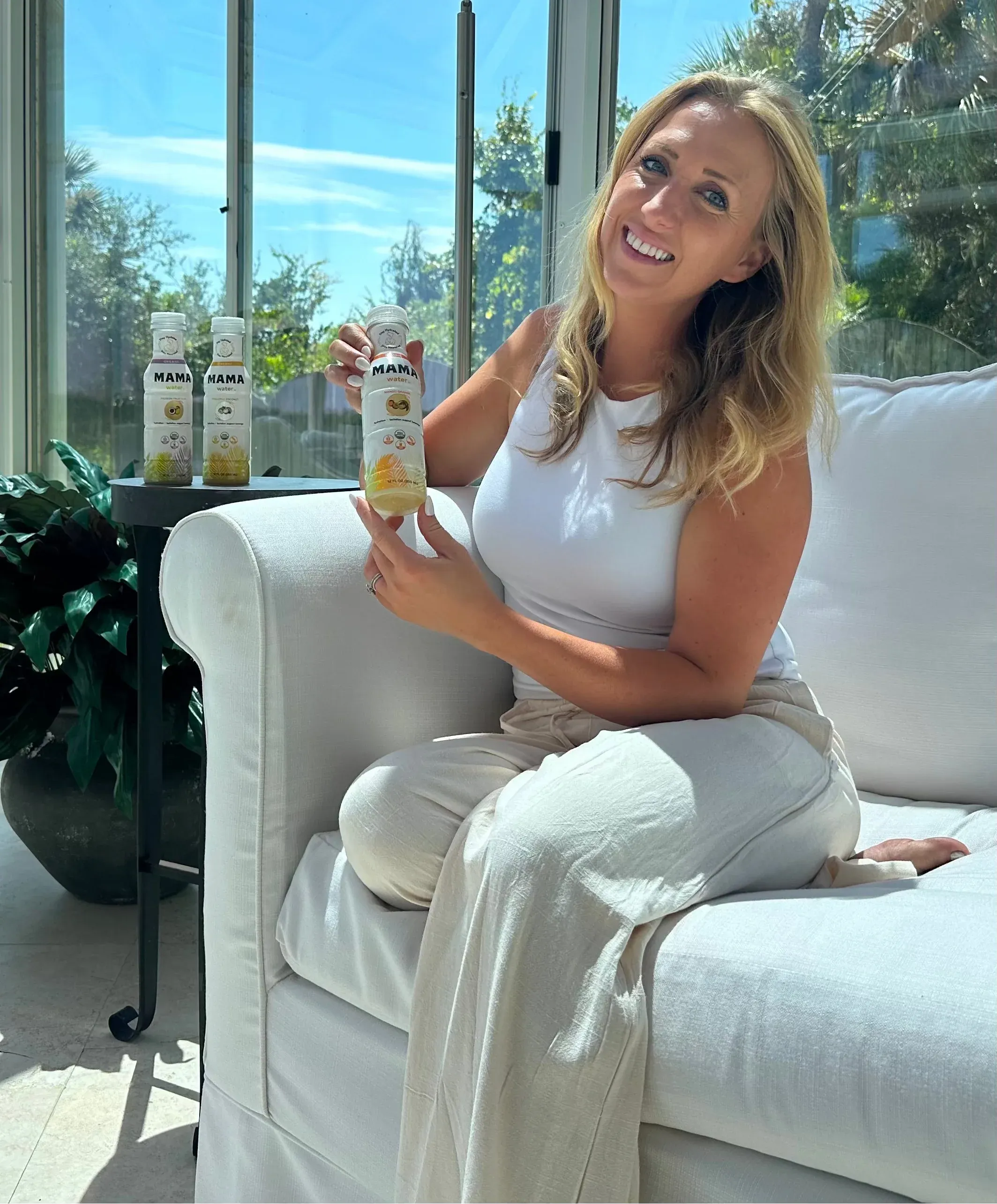 Amanda, founder of Mama Water, sitting on a white sofa holding a bottle of Mama Water