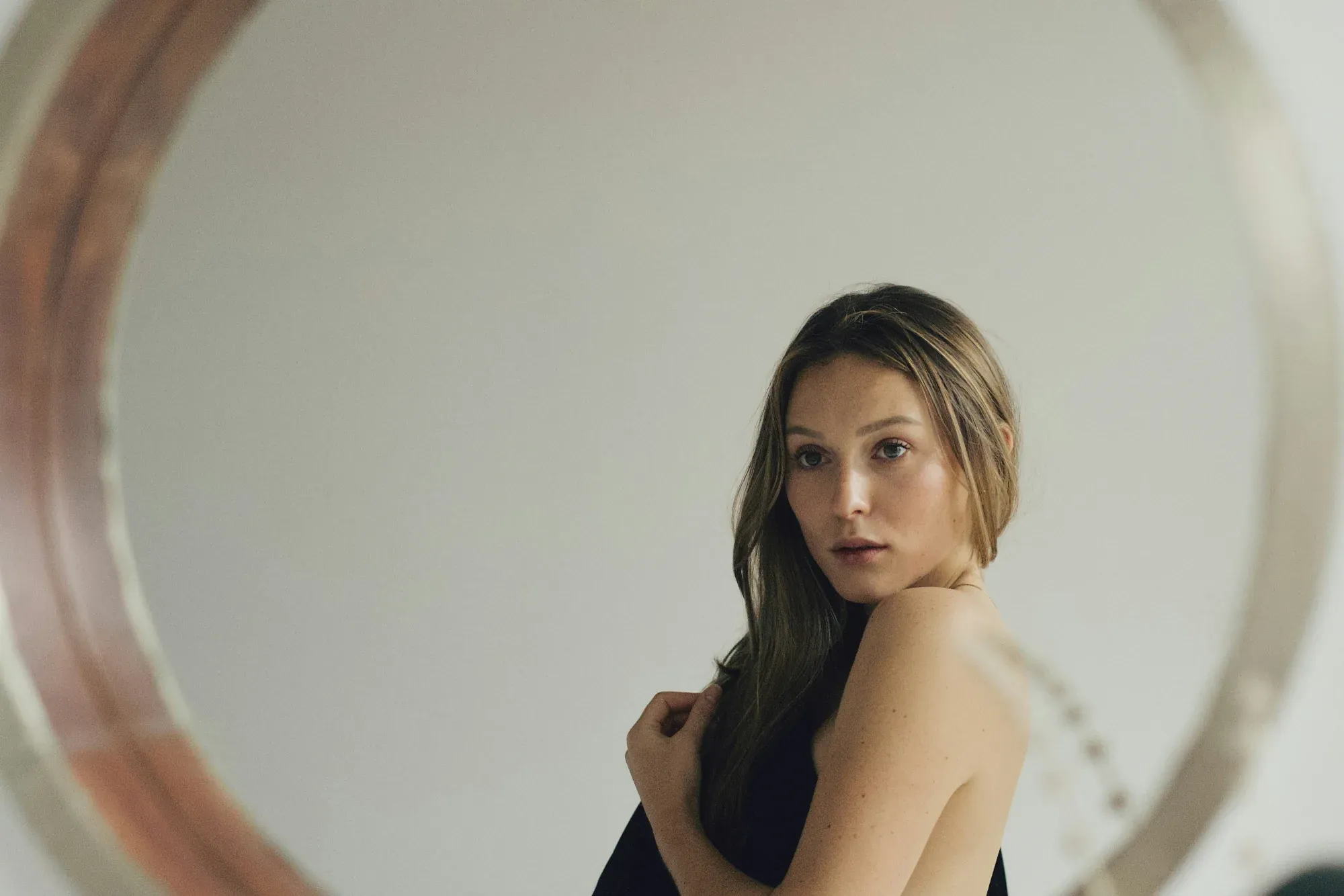 A woman in a black top reflected in a large round mirror, looking back over her shoulder