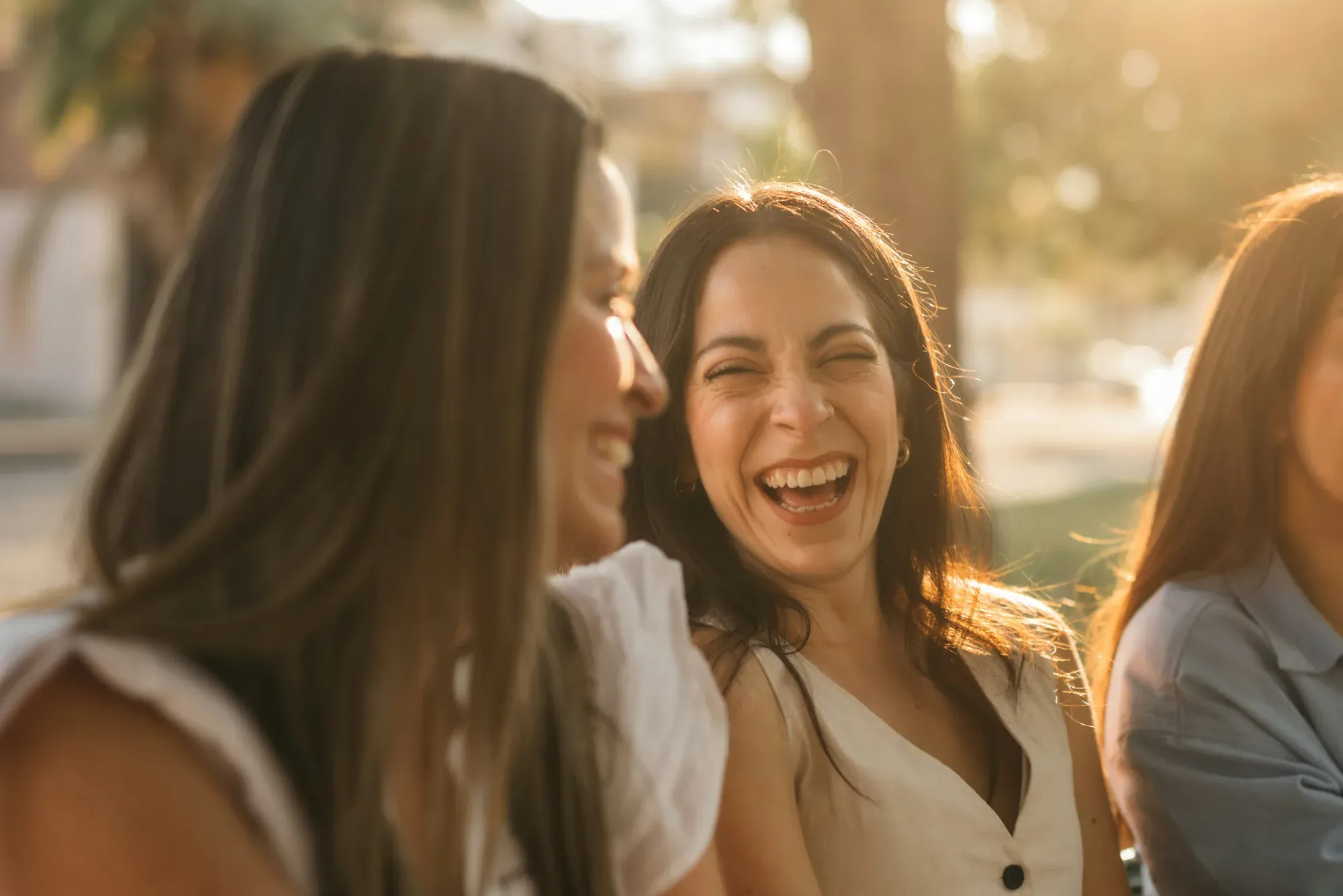 A woman laughing with her head thrown back among friends outdoors in warm golden-hour light