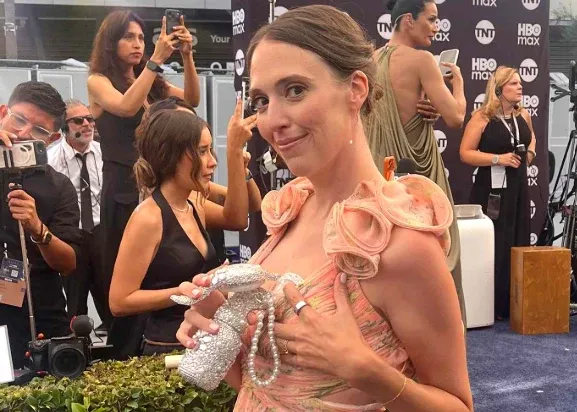 A woman on the Emmys red carpet in a gown, wearing a rhinestone-covered breast pump